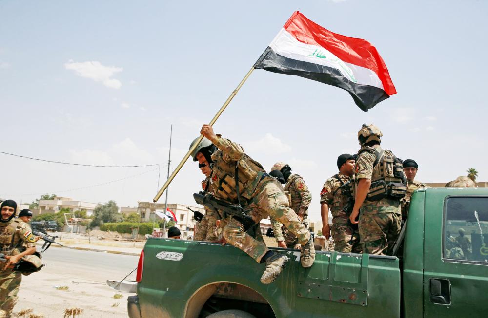 A soldier holds an Iraqi flag and jumps off a car before the start of a victory celebration after defeating Daesh militants in Mosul.
