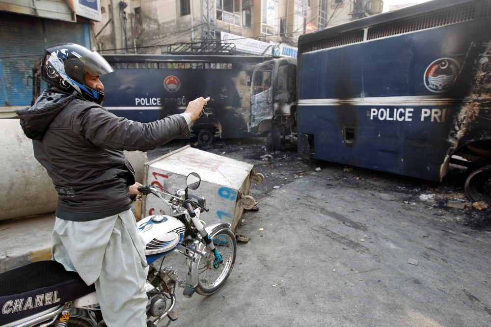 A passerby photographs police prison vans destroyed during clashes with protesters near the Faizabad junction in Islamabad, Pakistan, on Sunday. — Reuters
