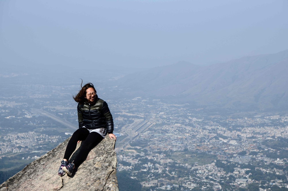 A woman poses on a rock on Hong Kong's highest peak Tai Mo Shan. Wooded hillsides, craggy ridges and wheeling birds of prey are a world away from Hong Kong's famous skyscrapers but the city's country parks are a necessary balm for its stressed out residents. - AFP