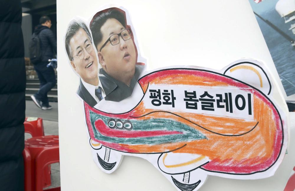 Pictures of South Korean President Moon Jae-in, left, and North Korean leader Kim Jong Un are seen on a sign during a rally to denounce the United States' policy against North Korea and demand the peaceful Winter Olympics in Seoul, South Korea, Tuesday. North Korea's delegation to the Winter Olympics in South Korea will include a 140-member art troupe, the two sides agreed Monday, while discussions continue over fielding a joint women's hockey team. The letters read 