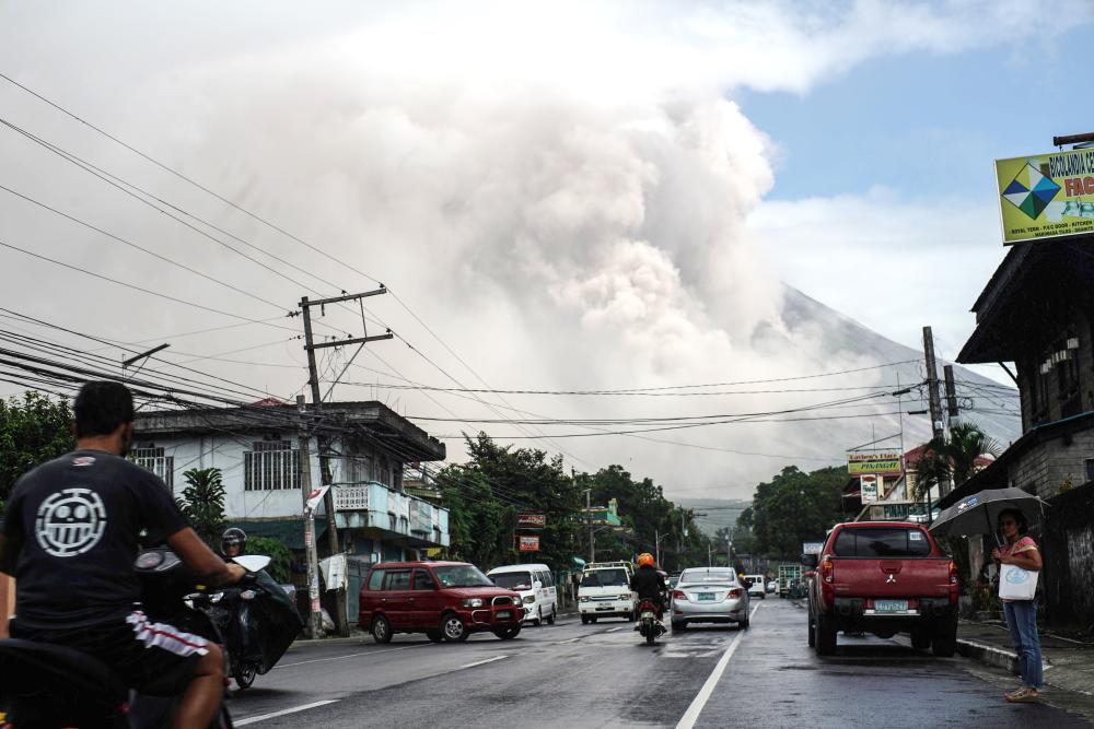 Motorists travel on a highway as Mount Mayon shot up a giant mushroom-shaped cloud as it continues to erupt near Camalig town, near Legazpi City in Albay province, south of Manila, Tuesday. — AFP