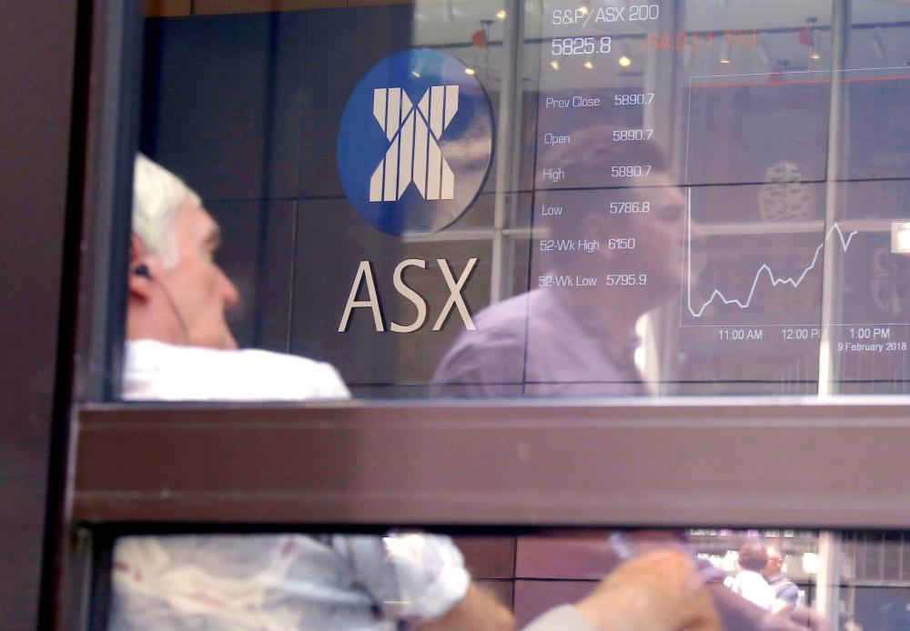 A pedestrian is reflected in a window where an investor sits looking at a board displaying stock prices at the Australian Securities Exchange (ASX) in Sydney, Australia, in this Feb. 9, 2018 file photo. — Reuters