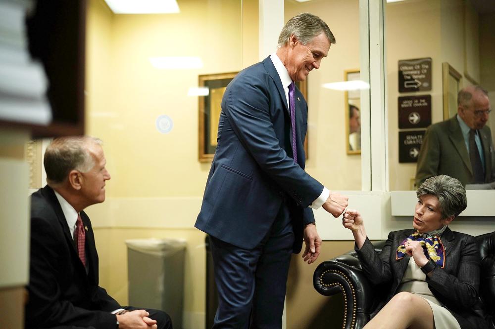 US Sen. David Perdue, center, fist-bumps Sen. Joni Ernst, right, as Sen. Thom Tillis looks on prior to a news conference on immigration at the Capitol in Washington on Monday. — AFP