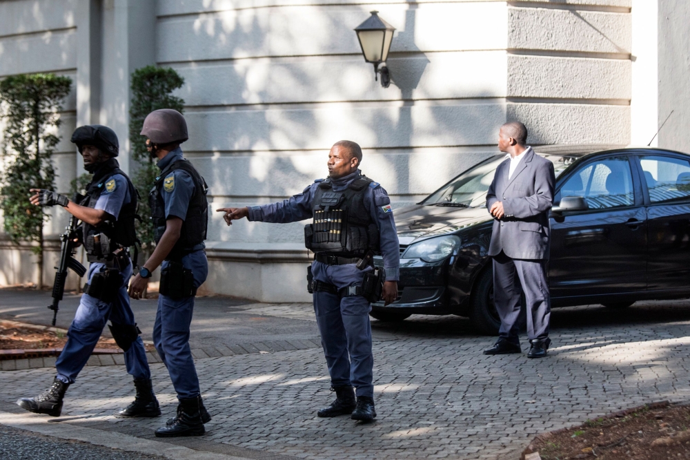 An armed South African Police member gestures as he leaves with colleagues the compound of the controversial business family Gupta while cars belonging to the Hawks, The Directorate for Priority Crime Investigation, are stationed outside, in Johannesburg, in this Feb. 14, 2018 file photo. — AFP