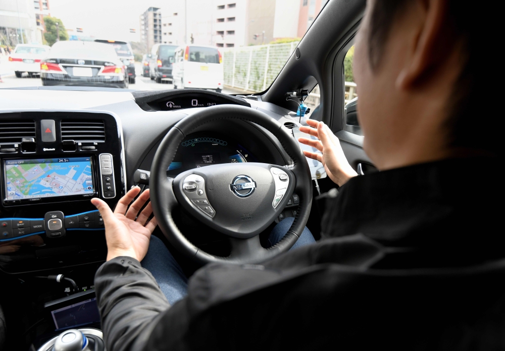 This photo taken on February 21, 2018 shows a man unlocking doors of a Nissan electric vehicle Leaf equipped with an auto-driving system controlled with exclusive software for smart phones, during a field test press preview in Yokohama, Kanagawa prefecture. Nissan and information technology company DeNA announced on February 23 that they will begin a field test of Easy Ride, the robo-vehicle mobility service being developed by both companies, from March 5 until March 18. / AFP / Toru YAMANAKA
