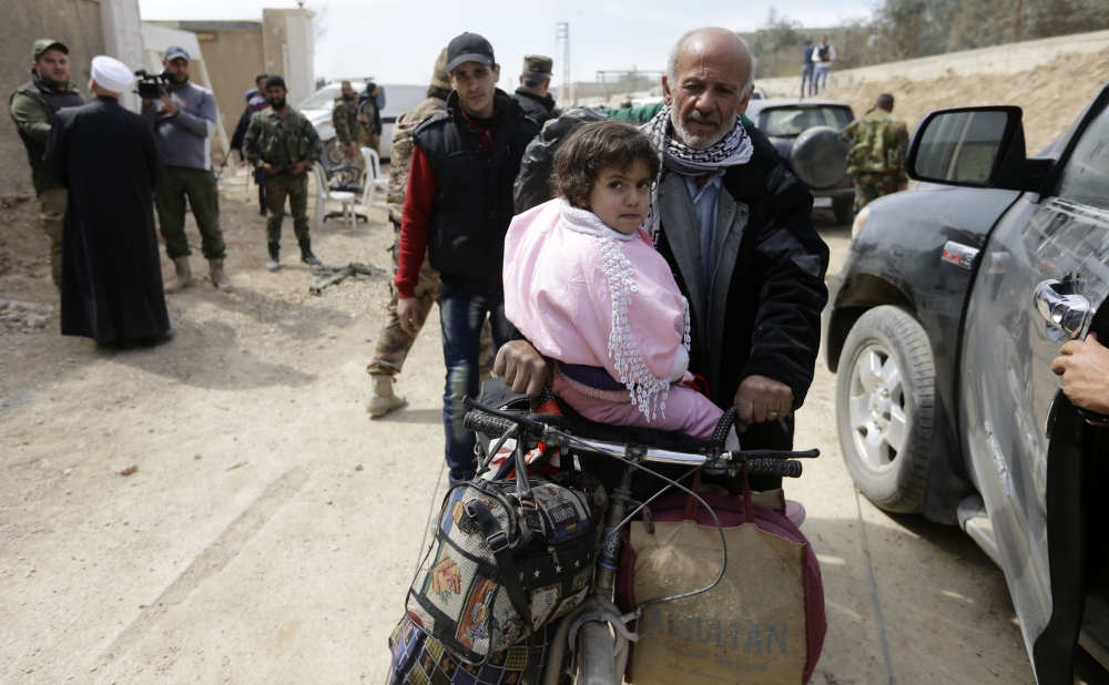 A Syrian man pushes a bicycle loaded with belongings and with a girl sitting on the handlebar while evacuating with other civilians through the regime-controlled corridor opened by government forces in Hawsh Al-Ashaari, east of the Eastern Ghouta enclave town of Hamouria on the outskirts of the capital Damascus, on Thursday. — AFP