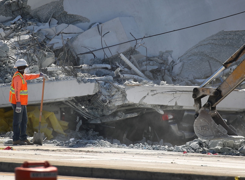 A crushed vehicle is seen near a worker as law enforcement and members of the National Transportation Safety Board investigate the scene where a pedestrian bridge collapsed a few days after it was built in Miami, Florida, on Friday. — AFP