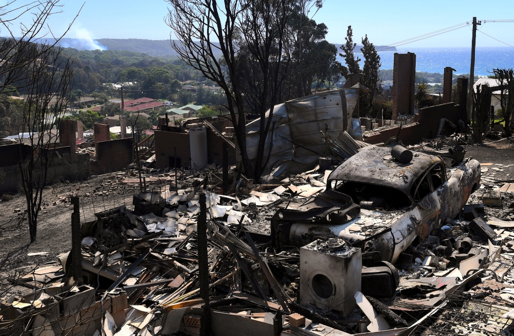 Smoke rises near a destroyed car and home after a bushfire swept through the town of Tathra, located on the southeast coast of New South Wales in Australia, on Monday. — Reuters