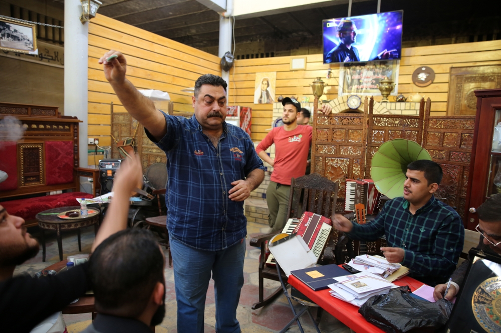 A man holds up a preserved coin specimen during a historical relic auction at the Moudallal cafe, Arabic for 