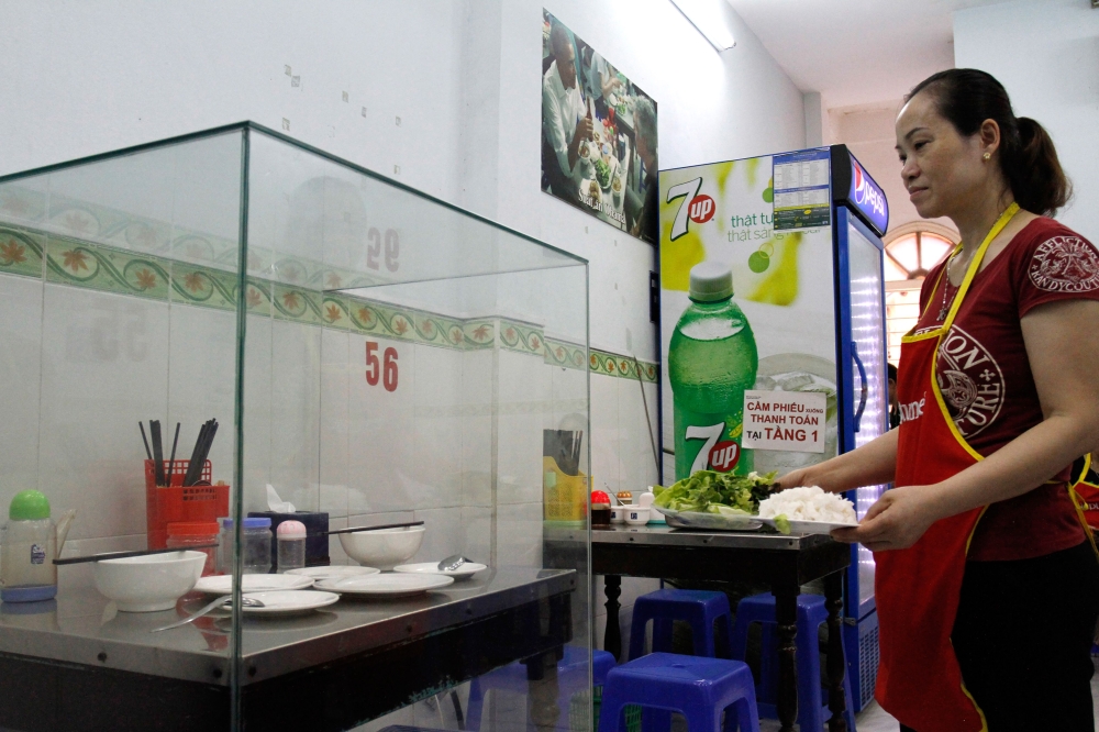 A waitress carries dishes to customers next to the glass-encased table where former US President Barack Obama sat at for a meal with chef Anthony Bourdain at Bun Cha Huong Lien restaurant, now dubbed 