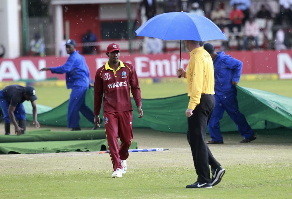 Groundsmen cover the pitch after the cricket world cup qualifier match between West Indies and Scotland was rain stopped at Harare Sports Club Wednesday. — AP