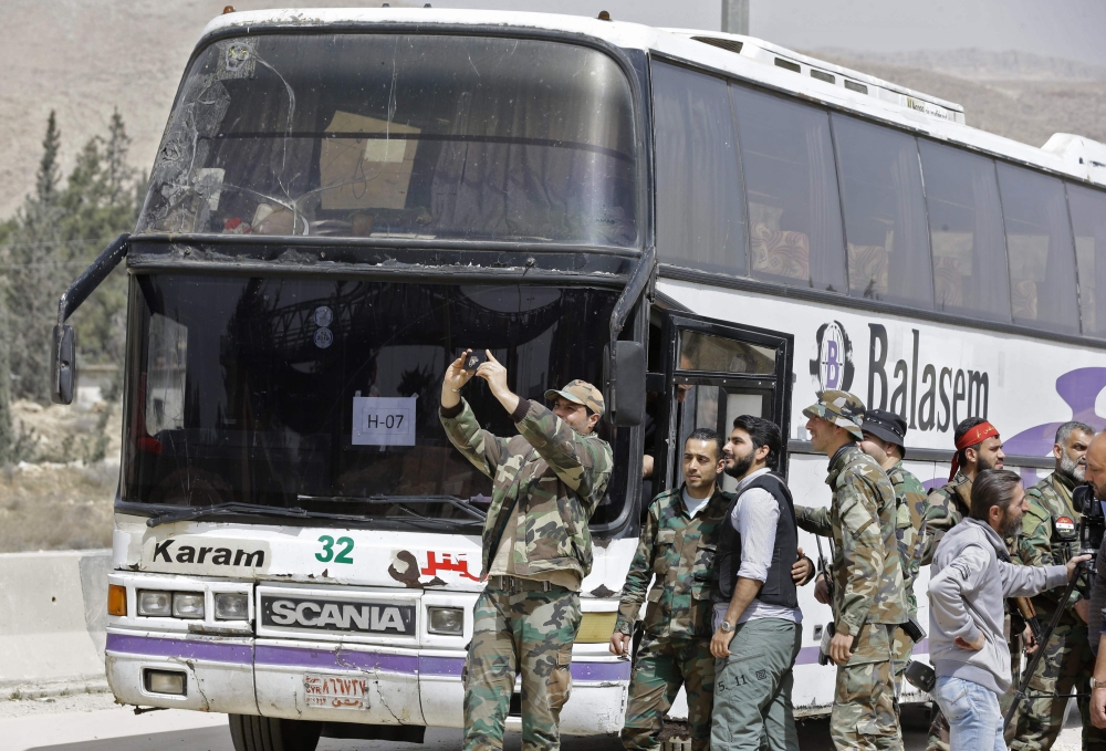 Syrian regime forces stand near buses waiting at the entrance of Harasta in Eastern Ghouta, on the outskirts of Damascus, on Thursday, after a deal was struck with the rebels in the area to evacuate the town. — AFP