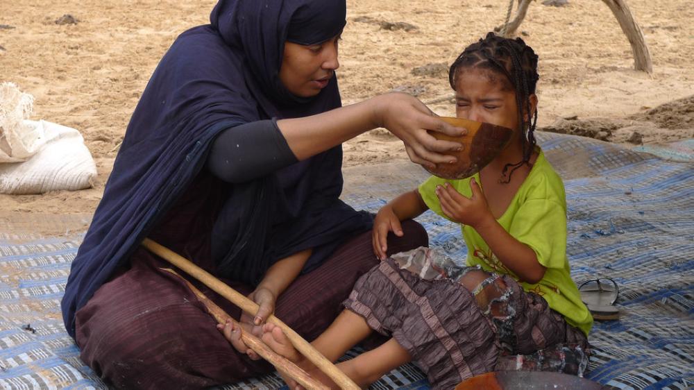 A “fattener” is shown forcefully feeding a young girl as she squeezes her feet between two sticks. The practice of force feeding is known as gavage - a French term used to describe fattening up geese to produce foie gras.
