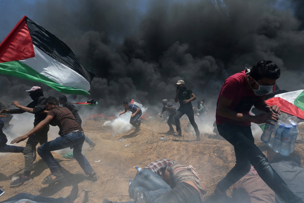Palestinians run for cover from Israeli fire and tear gas during a protest against US embassy move to occupied Jerusalem on Monday. — Reuters