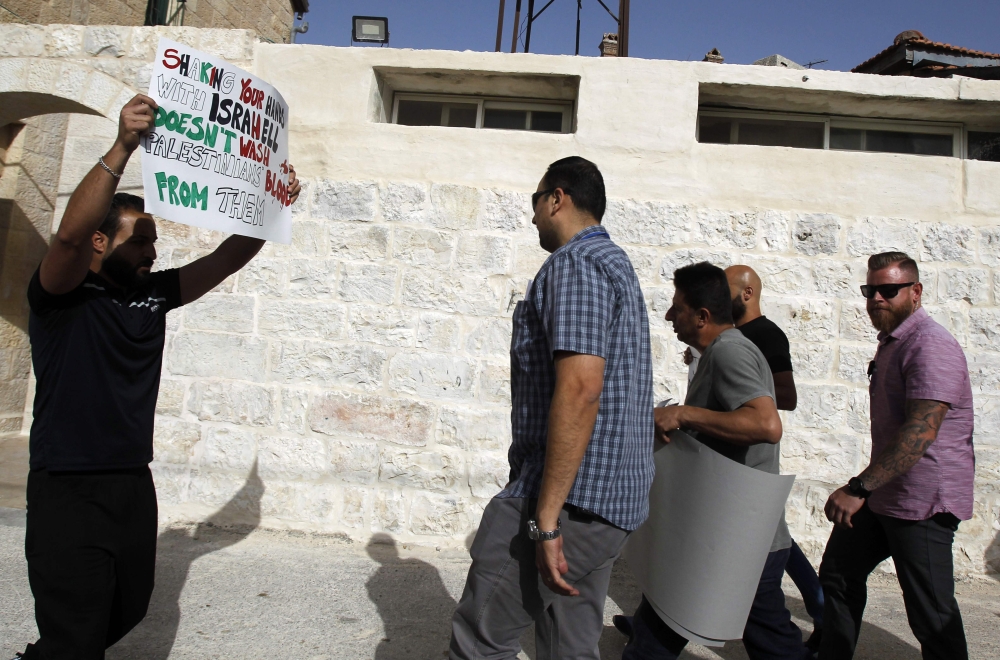 Palestinian men hold banners with political messages as they confront members of a US delegation (C and R), believed to be from the US consulate in occupied Jerusalem, near an event space in Beit Jala in the occupied West Bank on Tuesday. — AFP