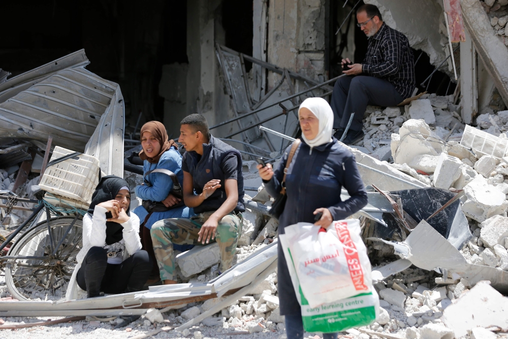 Civilians sit in the rubble of their former neighborhood following a flag raising ceremony at the entrance of Hajar Al-Aswad on the southern outskirts of the capital Damascus on Thursday, after the regime seized the Yarmuk Palestinian camp and adjacent neighborhoods of Tadamun and Hajar al-Aswad from the Daesh group. — AFP