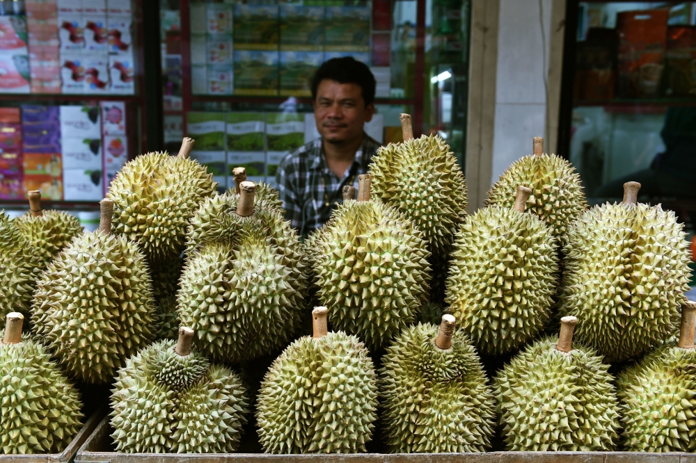 A Thai fruit vendor waits for customers behind a diplay of durians in Bangkok on Saturday. - AFP