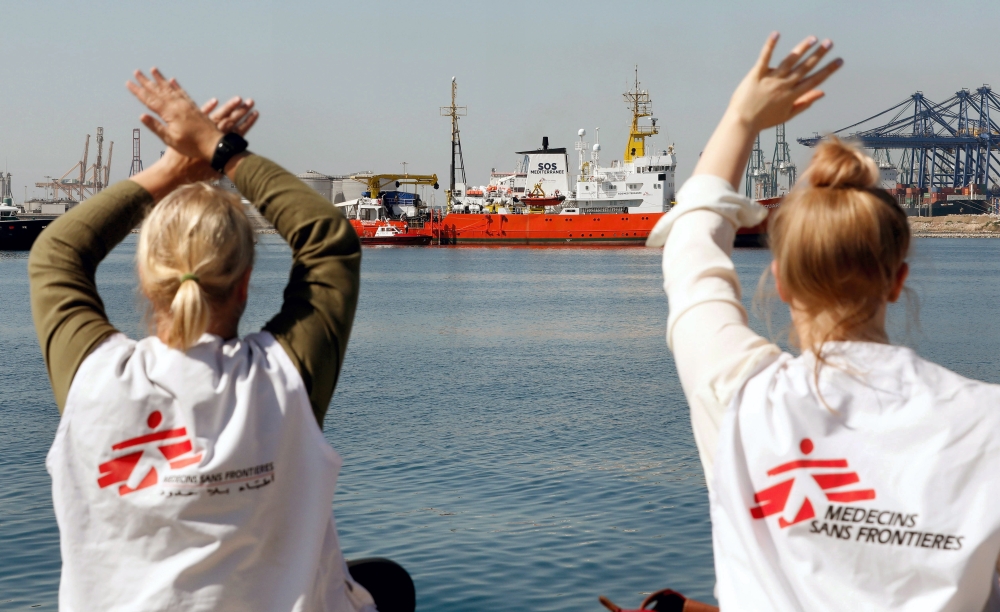 Two women wearing shirts of the relief organization Medecins Sans Frontieres wave to the Aquarius, background, aboard which 106 migrants were traveling as she enters the port of Valencia, Spain, on Sunday. — EPA