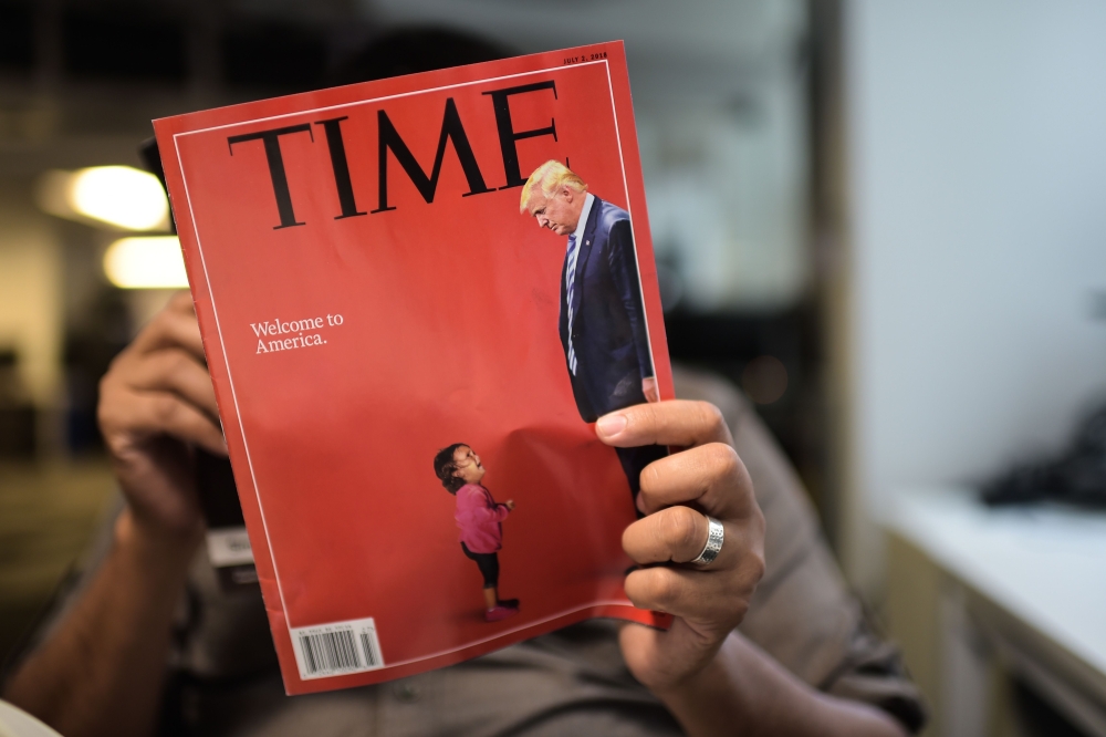A AFP journalist reads a copy of Time Magazine with a front cover using a combination of pictures showing a crying child taken at the US Border Mexico and a picture of US President Donald Trump looking down in Washington D.C., on Friday. — AFP 