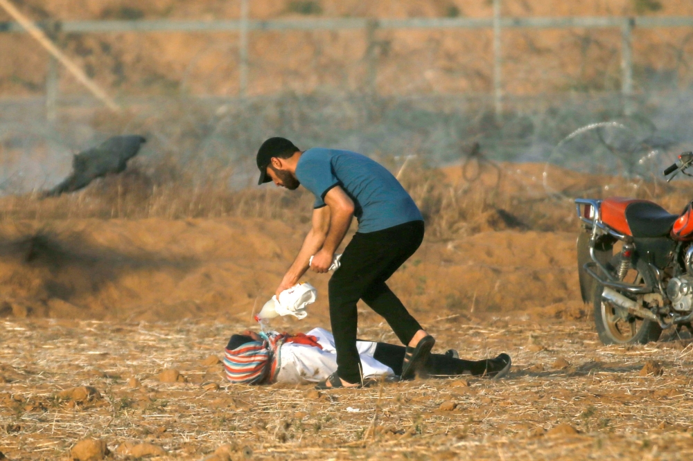 A Palestinian helps a woman injured by Israeli forces along the border between the Gaza Strip and Israel, east of Khan Yunis. — AFP