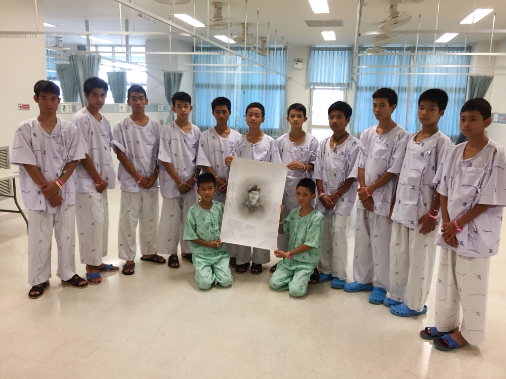 This handout photo released by the Ministry of Health, Chiang Rai Prachanukroh Hospital on Sunday shows members of the rescued “Wild Boars” football team at hospital in Chiang Rai province posing after writing messages on a drawing of former Navy SEAL diver Saman Kunan who died on July 6 during the rescue mission. — AFP
