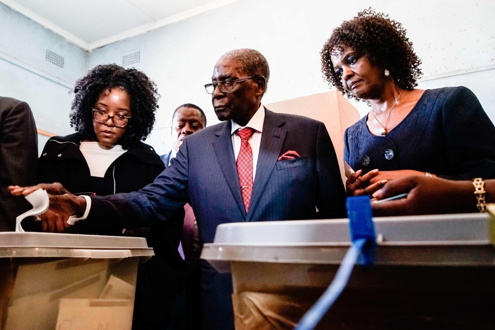 Former Zimbabwean president Robert Mugabe, center, is watched by his daughter Bona, left, and wife Grace as he casts his vote at a polling station located in a primary school in the Highfield district of Harare during the country’s general elections on Monday. — AFP