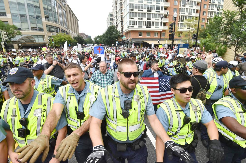 Police escort far-right demonstrators led by ‘Unite the Right’ organizer Jason Kessler, holding flag, during a rally at Lafayette Park opposite the White House in Washington, D.C. on Sunday, one year after the deadly violence at a similar protest in Charlottesville, Virginia. — AFP