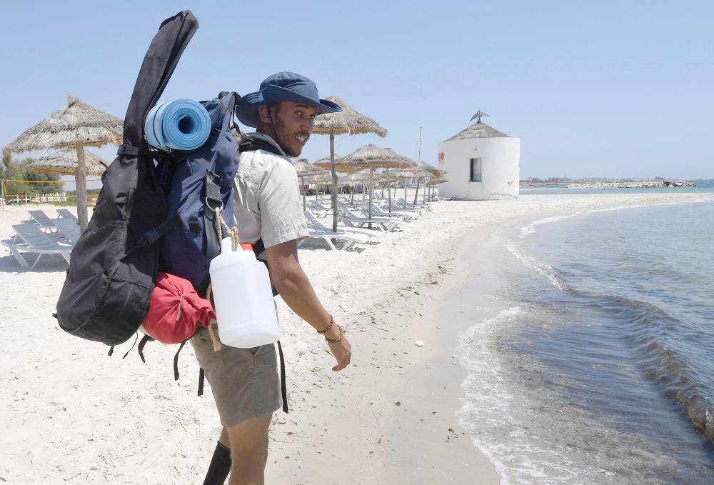 Mohamed Oussama carrying a backpack, his guitar and rubbish bags, walks along the Nabuel beach in northern Tunisia.  The 27-year-old engineer set out in July to walk a 300 km stretch of coast, cleaning up a string of 30 beaches along the way. — AFP