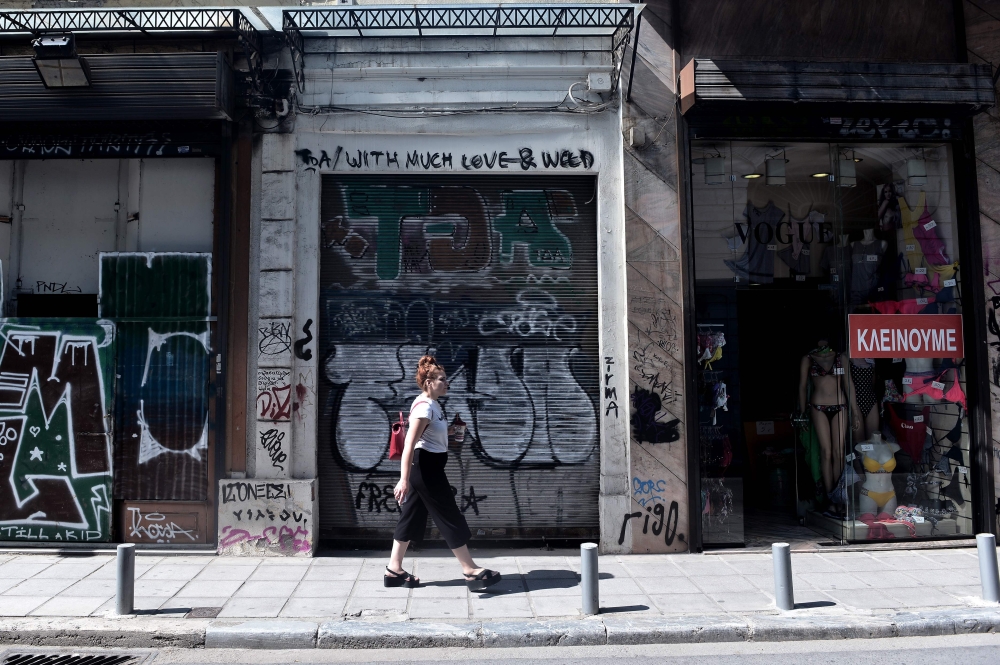 A woman walks past a closed shops and a shop displaying a poster reading 