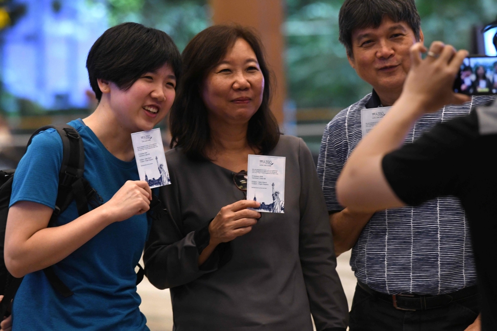 Singaporean William Chua, right, with family members, all passengers of flight SQ22, Singapore Airlines’ inaugural non-stop flight to New York pose with souvenir cards after their their check-in at Changi International Airport in Singapore on Thursday. — AFP
