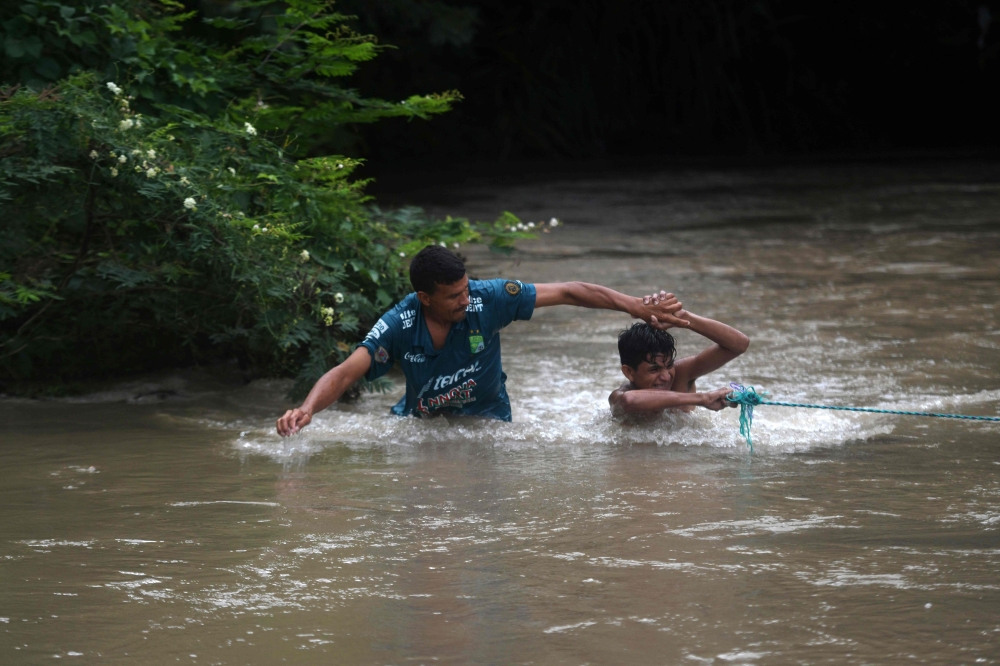 Honduran migrants attempt to cross the border Goascoran River to enter illegally to El Salvador, in Goascoran, Honduras, on Thursday. — AFP