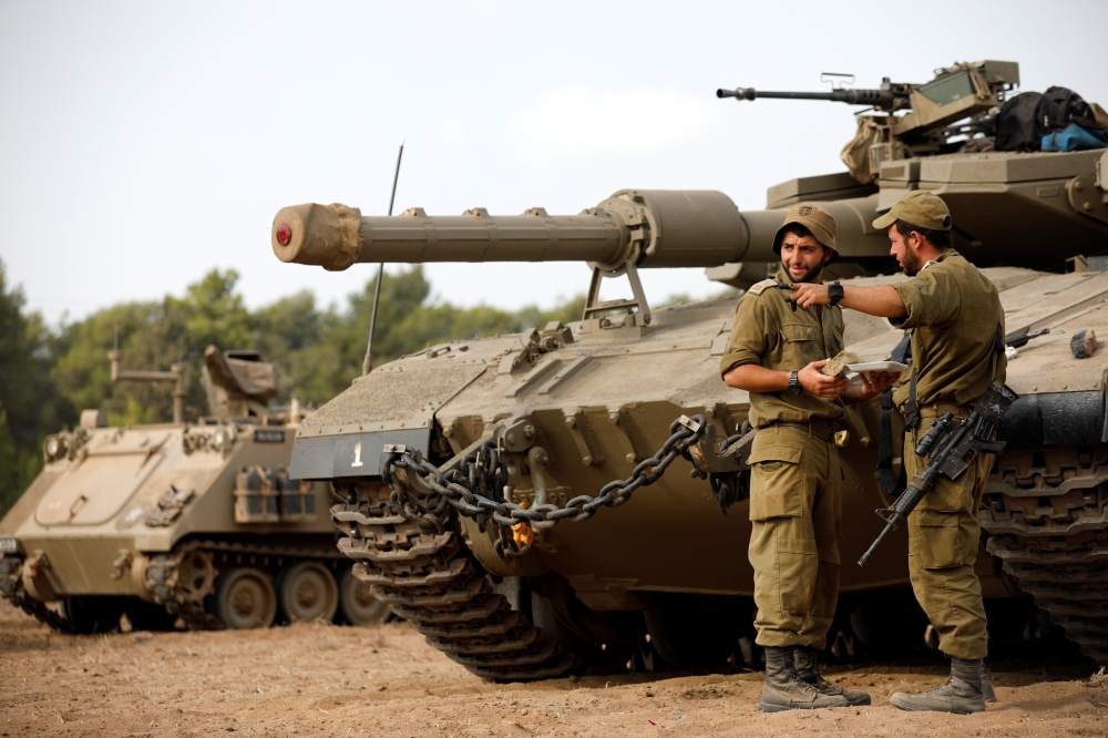 Israeli soldiers speak next to a tank as military armored vehicles gather in an open area near Israel’s border with the Gaza Strip on Thursday. — Reuters