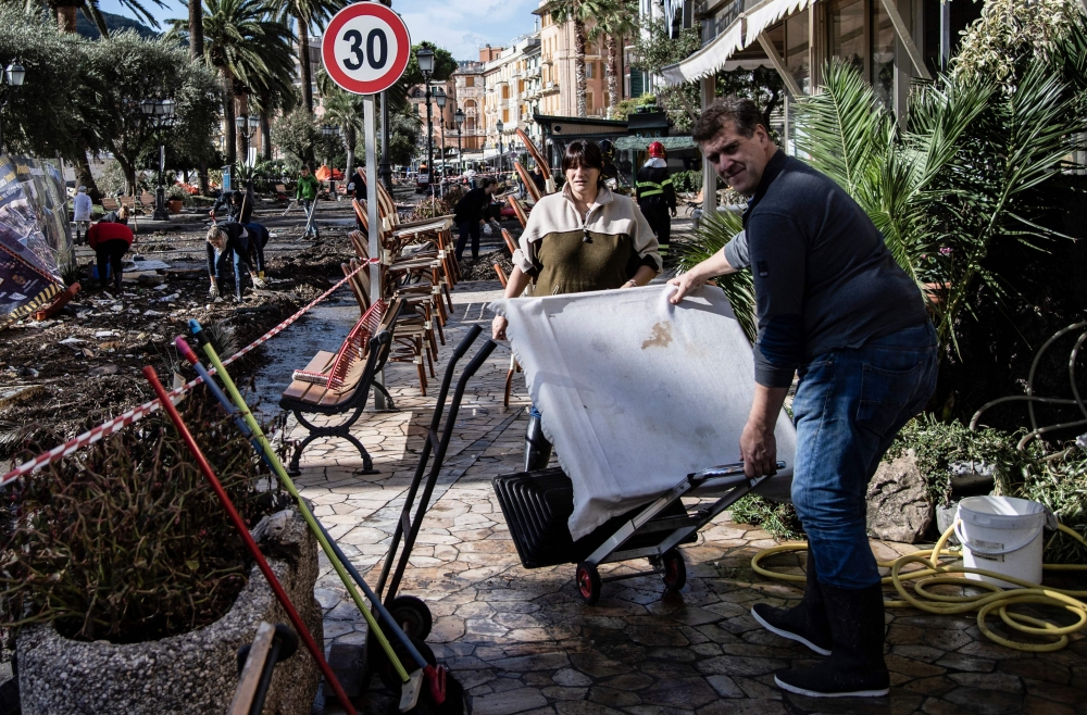 Two people carry an object as they walk through a destroyed street near the harbor of Rapallo, near Genoa, Italy, on Oct. 30, 2018, after a storm hit the region and destroyed a part of the dam the night before. — AFP