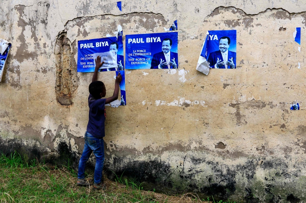 A young child holds posters of Cameroonian President Paul Biya on a wall in Yaoundé on Tuesday.  — AFP