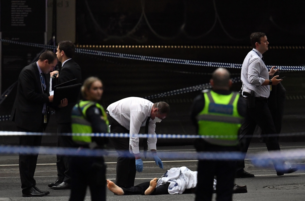 A police officer, center, inspects a body at the crime scene following a stabbing incident in Melbourne on Friday. — AFP