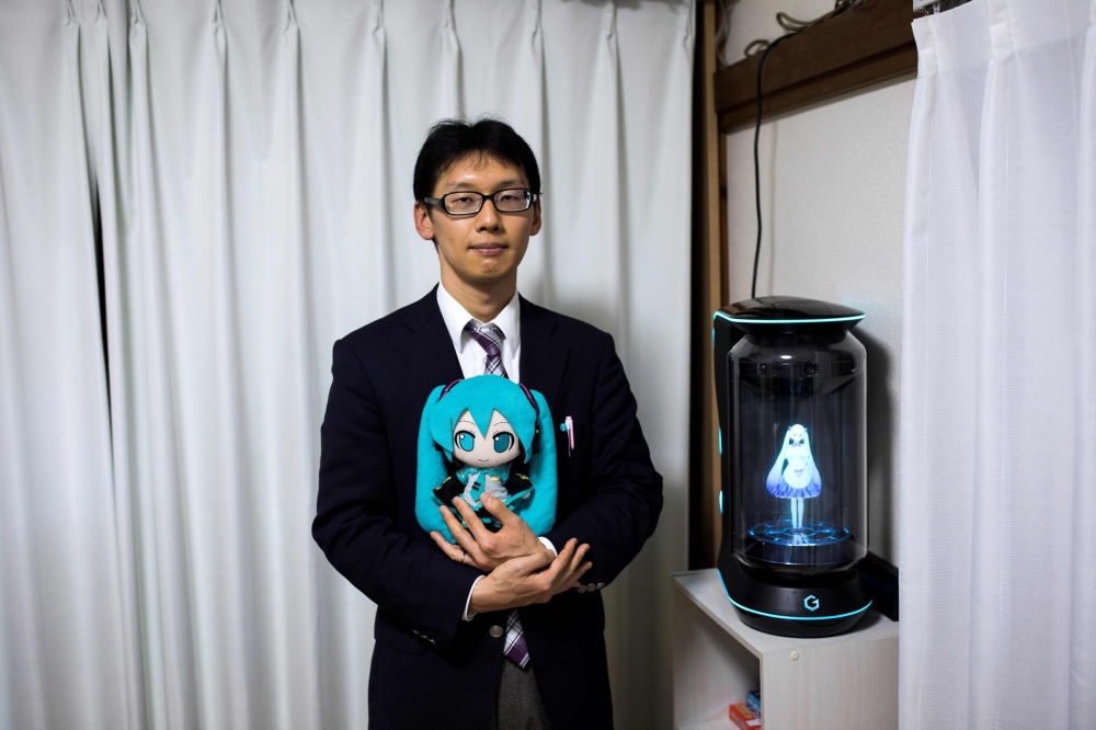 


Japanese Akihiko Kondo poses next to a hologram of Japanese virtual reality singer Hatsune Miku as he holds the doll version of her at his apartment in Tokyo, a week after marrying her, in this Nov. 10, 2018 file photo. — AFP