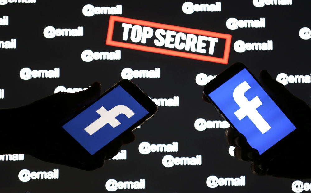 Persons hold smartphones with the Facebook logo in front of displayed 