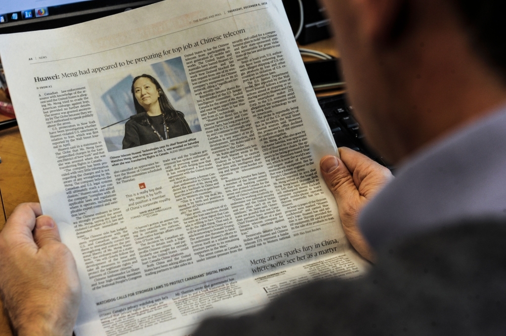 An illustration shows a journalist reading a news page about tech giant Huawei in The Globe and Mail in Montreal, Canada, Thursday. The arrest of a top executive of Huawei at the request of US authorities signals a toughening stand in Washington on dealing with Chinese tech firms amid longstanding concerns over cyberespionage. Meng Wanzhou (pictured on the news page), Huawei's chief financial officer, was detained this week in Canada and faces an extradition request from US authorities over an investigation into suspected Iran sanctions violations by the Chinese technology giant. — AFP