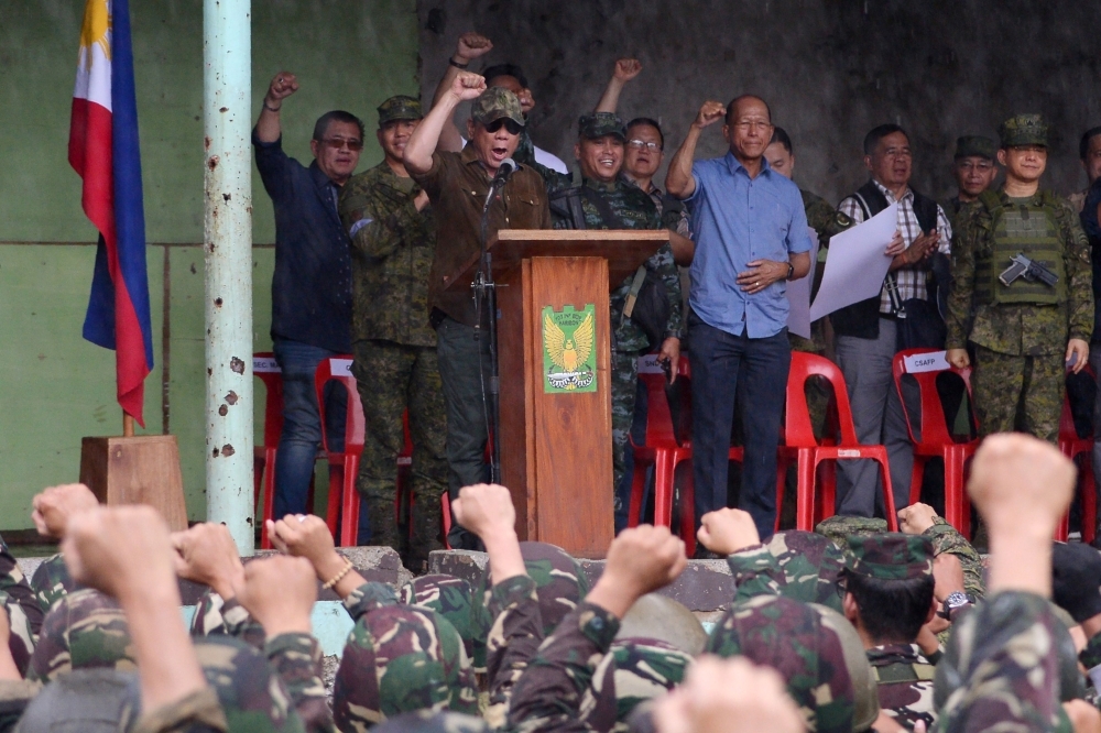 This file photo shows President of the Philippines Rodrigo Duterte (on stage in brown) raising a clenched fist along with soldiers during a ceremony in Bangolo district in Marawi. President Rodrigo Duterte on Friday asked legislators to extend martial law across the nation's southern third through the end of 2019 in order to quell the continuing violence in the unrest-prone region, officials said. — AFP