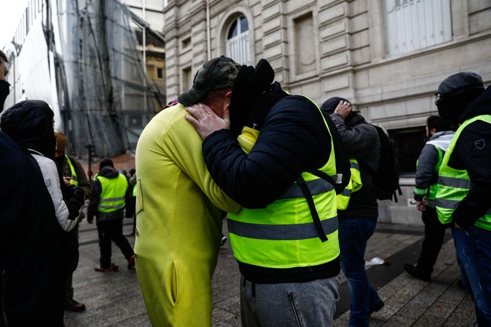 Protesters wearing yellow vests (Gilets jaunes) hug on the Champs Elysees in Paris on Saturday during a protest against rising costs of living they blame on high taxes. — AFP