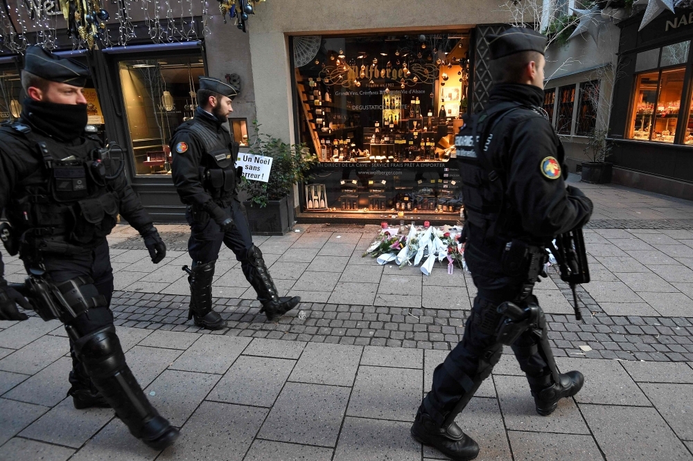 French gendarmes walk past flowers and candles laid in the street in tribute to the victims of a deadly shooting two days ago in central Strasbourg, France, on Thursday. — AFP