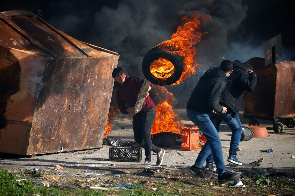 A Palestinian uses a piece of wood to move a burning tire during clashes with Israeli troops in Ramallah, near the Jewish settlement of Beit El, in the occupied West Bank on Thursday. — AFP