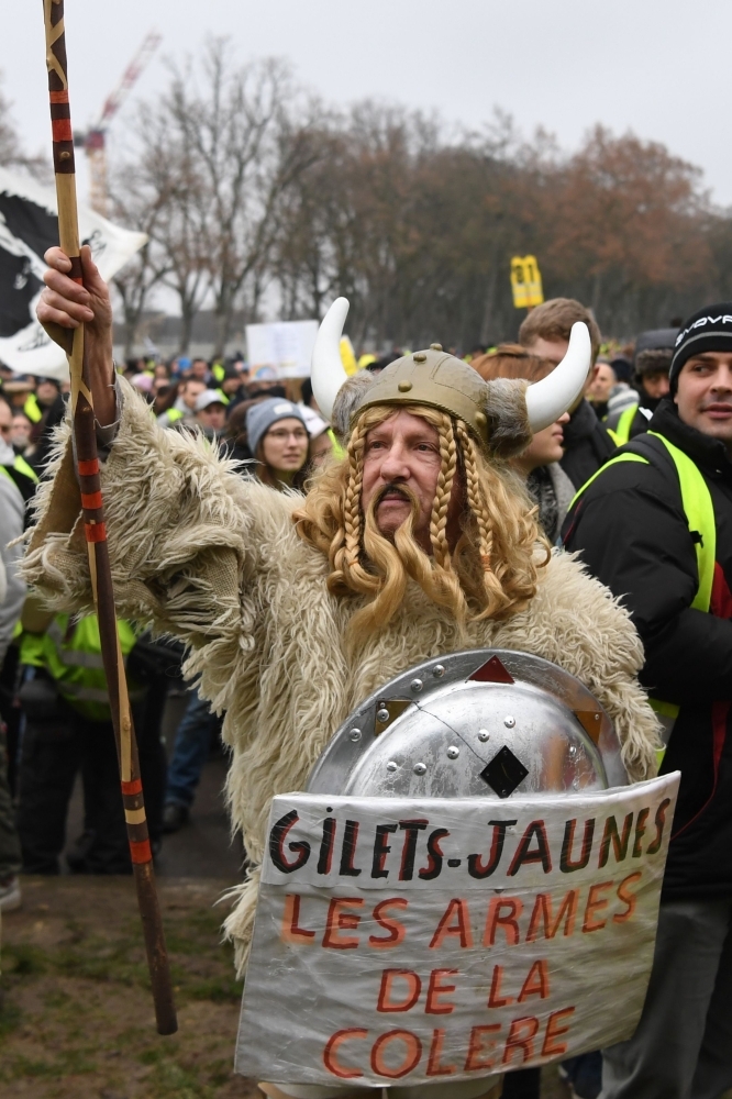 A demonstrator dressed as a Gaul holding a spear and a shield with a message reading 