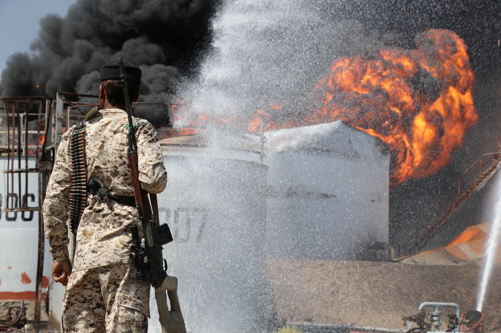 A soldier looks as fire engulfs an oil storage tank at the Aden oil refinery one day after an explosion in the refinery in Aden, Yemen on Saturday. — Reuters
