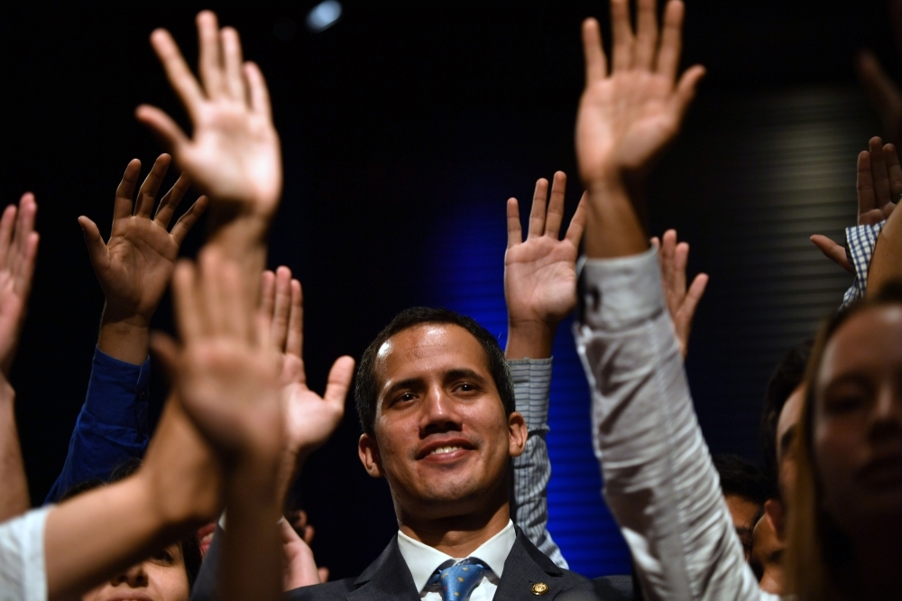Venezuelan National Assembly head and self-proclaimed acting president Juan Guaido, center, raises his hands surrounded by students after speaking at the Metropolitan University in Caracas on Monday. — AFP