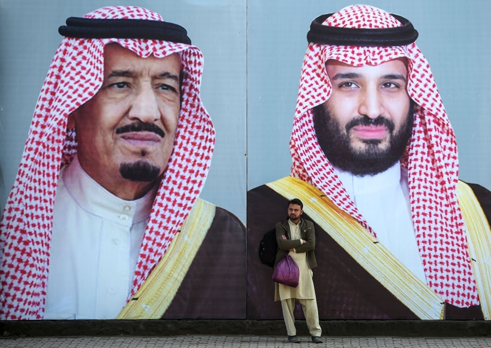 A Pakistani man waits for transport in front of billboards showing portraits of Custodian of the Two Holy Mosques King Salman and Crown Prince Muhammad Bin Salman displayed on a street ahead of the Crown Prince's arrival in Islamabad. — AFP