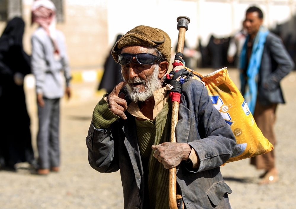 A Yemeni man walks carrying on his walking cane a bag of food aid provided by a local charity to affected families in Sanaa. — AFP