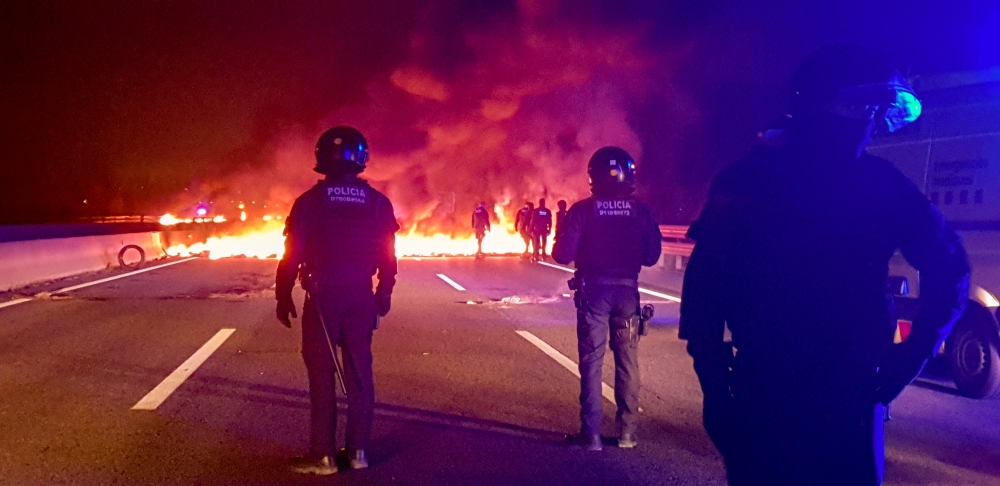 Police officers stand next to burning barricades settled to block the AP7 highway during a regional strike near Girona, Spain, on Thursday. — Reuters