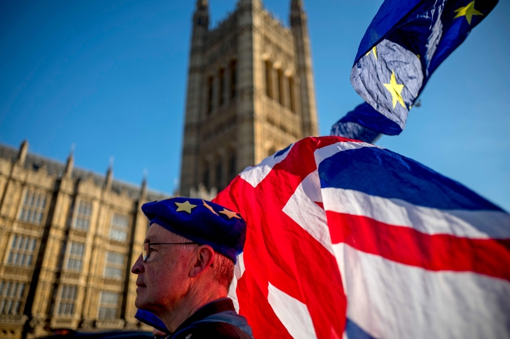 An anti-Brexit protester wearing a European Union flag cap, flies European and Union flags outside the Houses of Parliament in London, on Thursday. — AFP