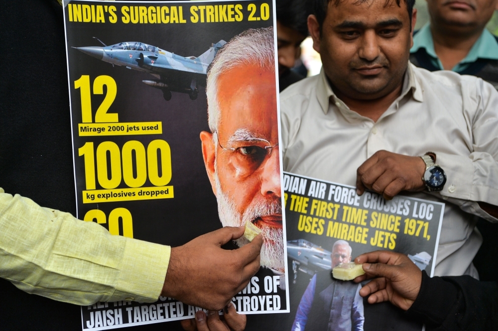 Supporters of Indian Prime Minister Narendra Modi offer sweets to a poster displaying his portrait in New Delhi on Tuesday, as they celebrate the Indian Air Force (IAF) strike launched on a Jaish-e-Mohammad (JeM) camp at Balakot, Pakistan. — AFP